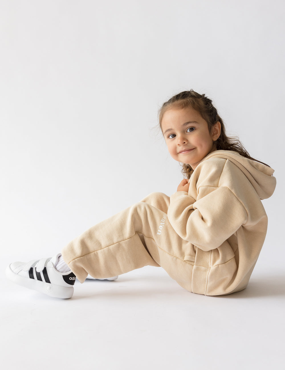 Kids beige sweatpants with 'heaven' logo print, worn during seated pose