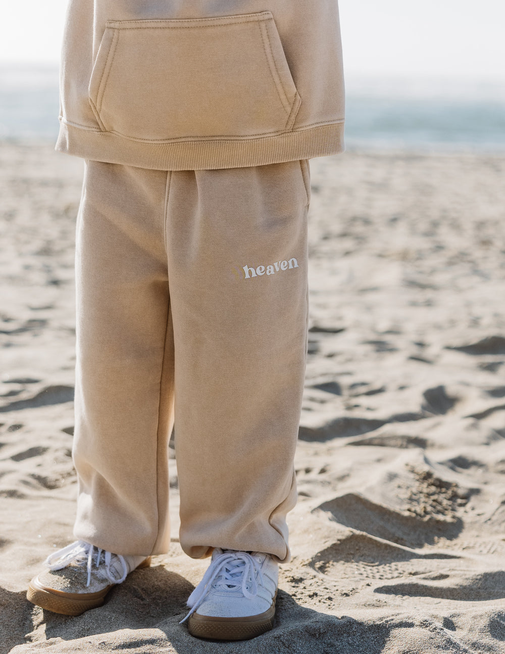 Beige kids sweatpants close-up with 'heaven' logo on the leg and cuff