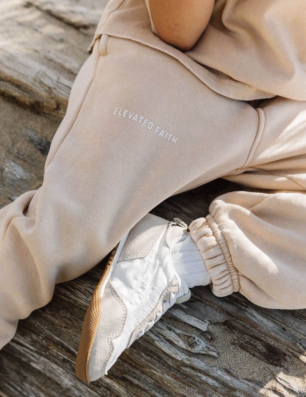 Beige kids sweatpants with 'ELEVATE' and 'FAITH' text print on the leg