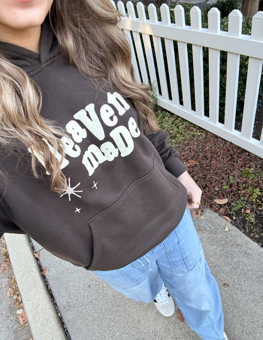 Unisex hoodie close-up showing dark brown fabric and “Heaven Made” logo print.