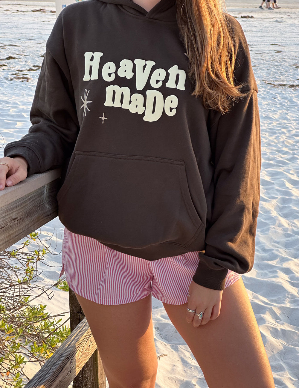 Unisex hoodie in dark brown with “Heaven Made” chest print and front pocket.