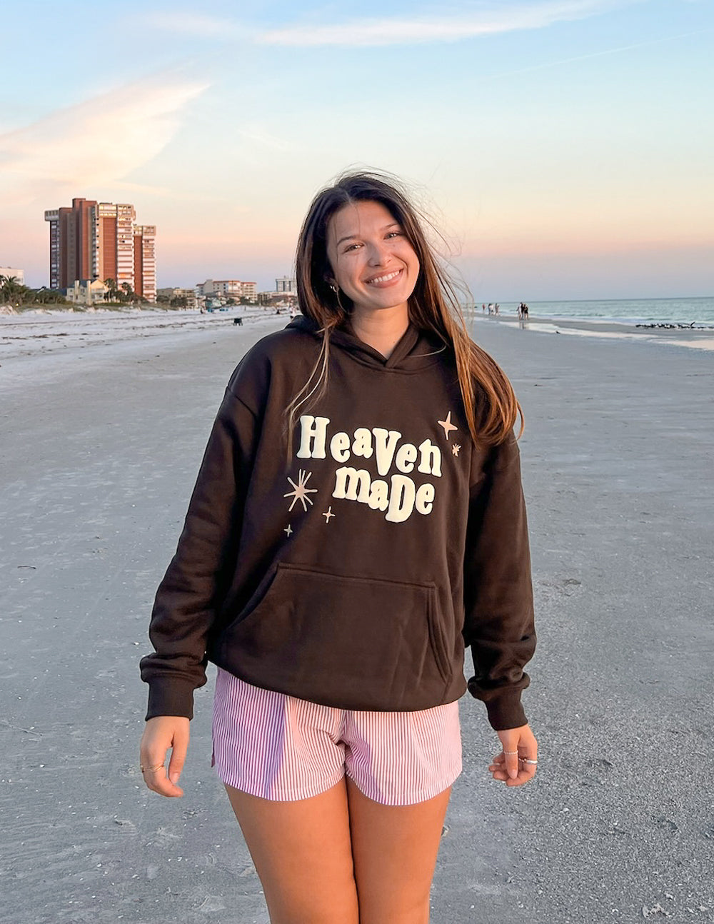 Dark brown unisex hoodie with hood and “Heaven Made” logo; relaxed standing fit.