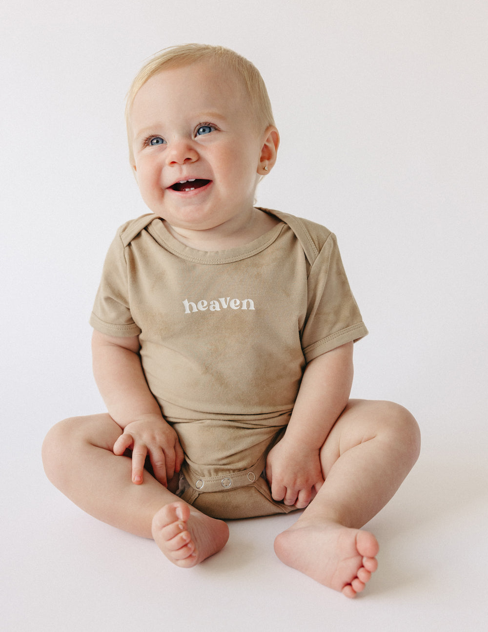 Tan baby onesie with 'heaven' chest print, short sleeves and crew neck