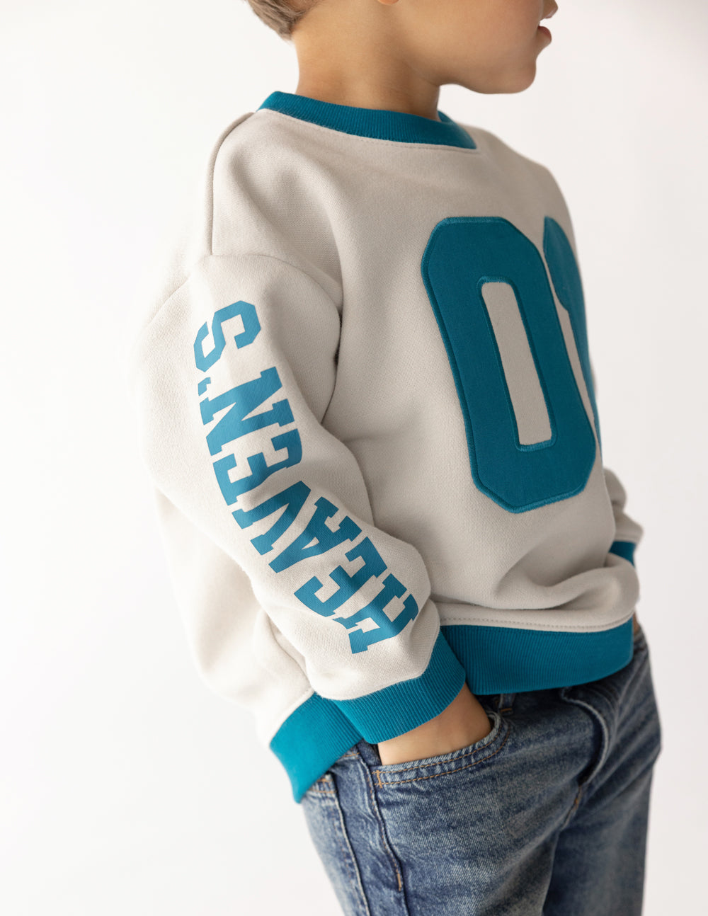 Kids crewneck sweatshirt side view in cream with teal number 01 and sleeve lettering