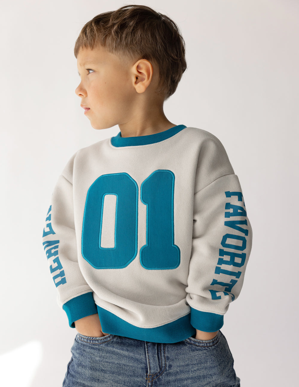 Kids crewneck sweatshirt back view in cream with teal 01 graphic and sleeve text
