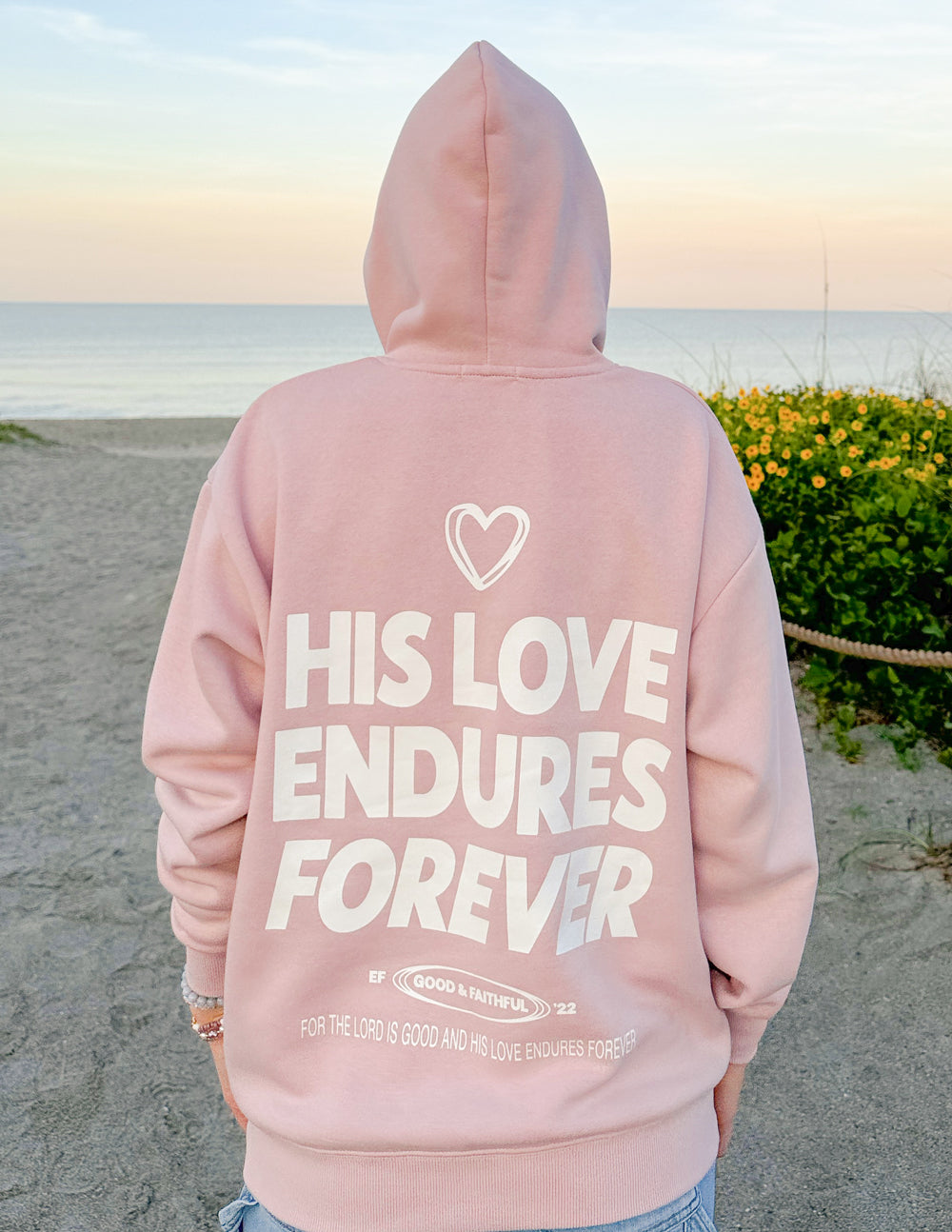 Unisex pink hoodie, back shows heart and “HIS LOVE ENDURES FOREVER” print