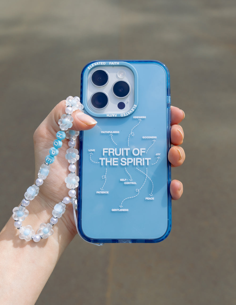 Blue Fruit of the Spirit phone case in hand with bracelet; clear back and camera cutouts