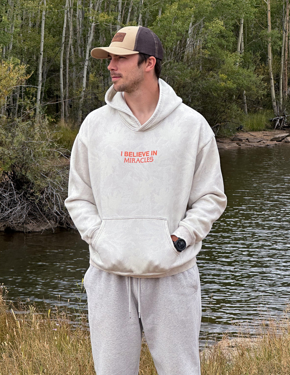 Unisex light gray hoodie with orange 'I Believe in Miracles' chest graphic