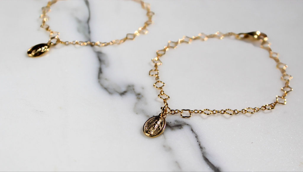 Two gold children’s charm bracelets with oval medal pendants on marble.