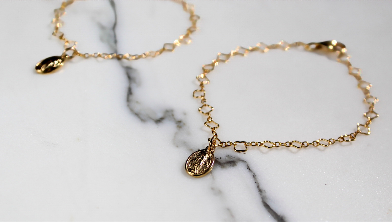 Two gold children’s charm bracelets with oval medal pendants on marble.