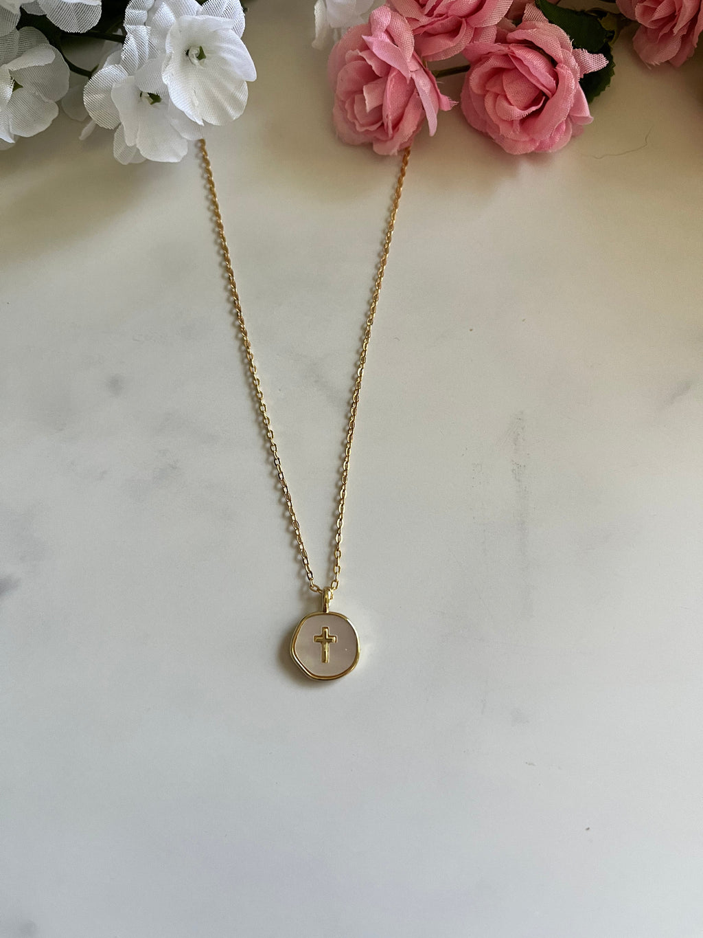 Gold cross pendant necklace with a round charm and thin chain, laid in a V shape