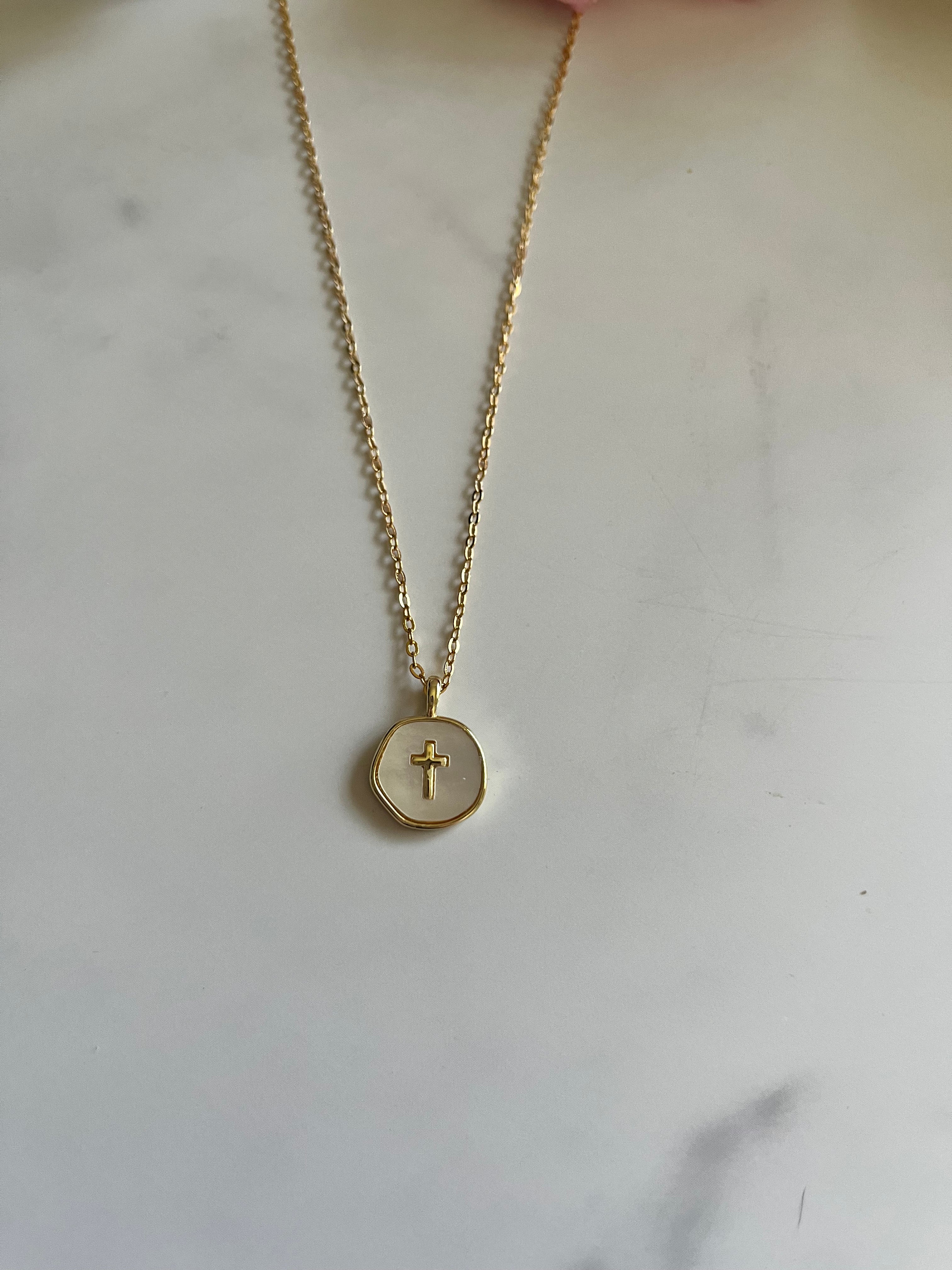 Gold cross pendant necklace with round charm on a thin chain, close-up