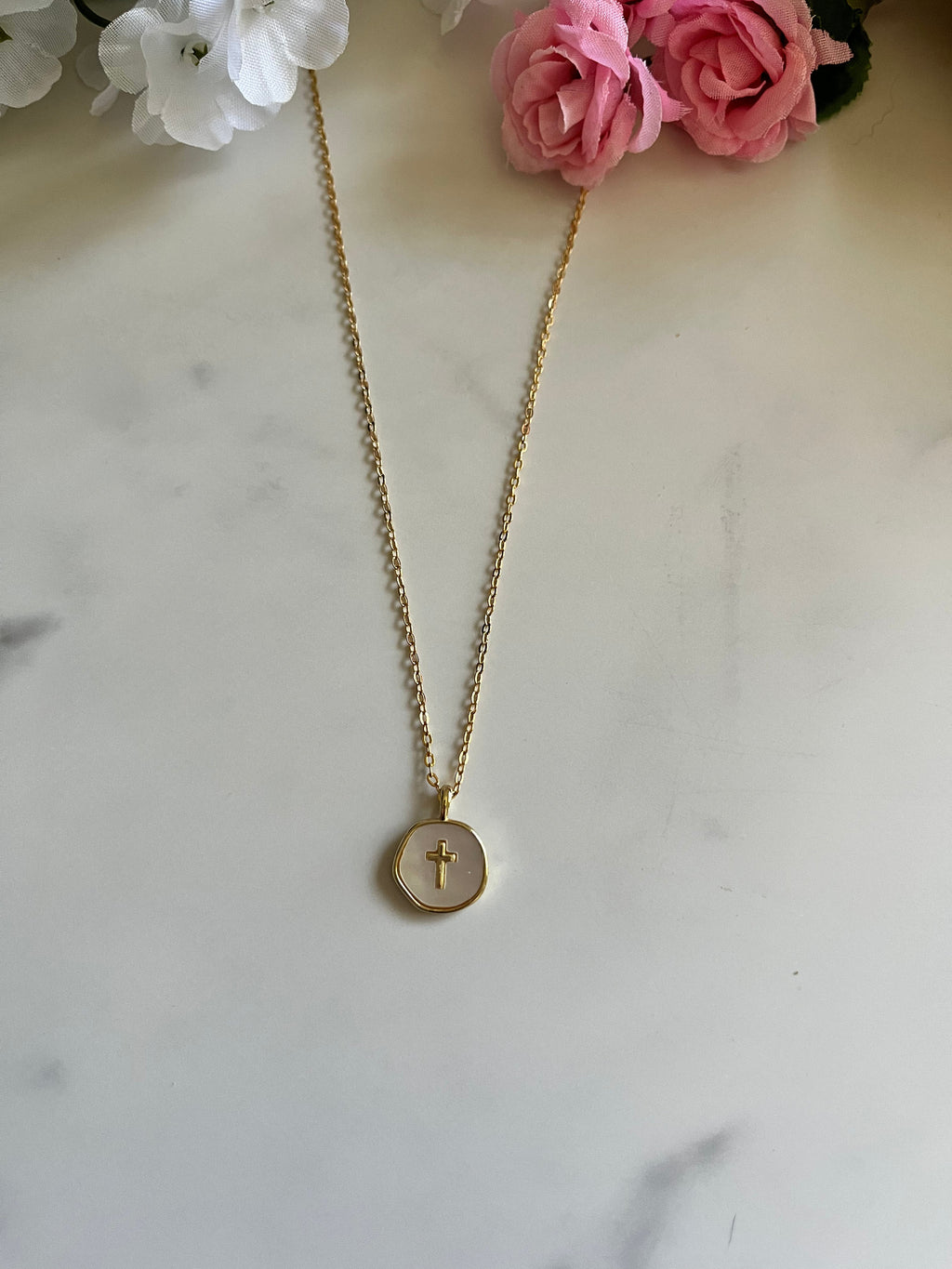 Gold necklace with round pendant featuring a cross charm on a thin chain
