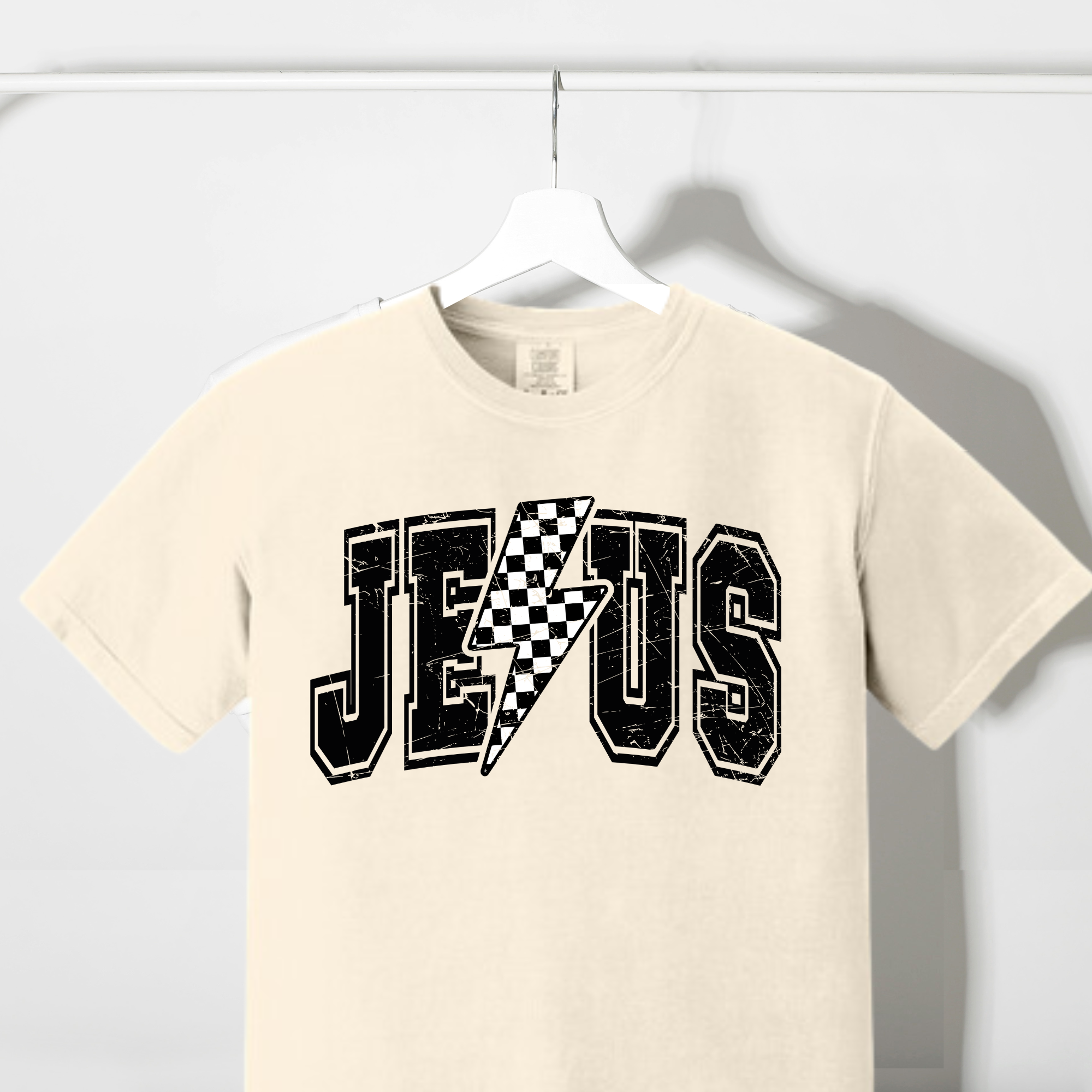 Cream graphic T-shirt with checkered lightning bolt and 'Jesus' text