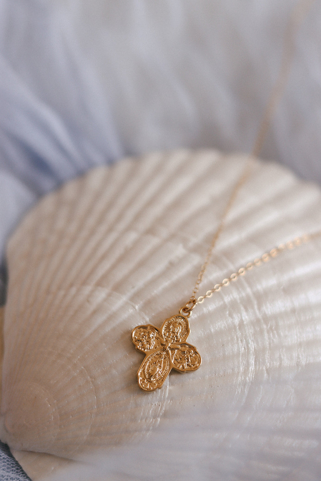 Gold-tone cross pendant necklace with delicate chain, three-lobed cross charm.