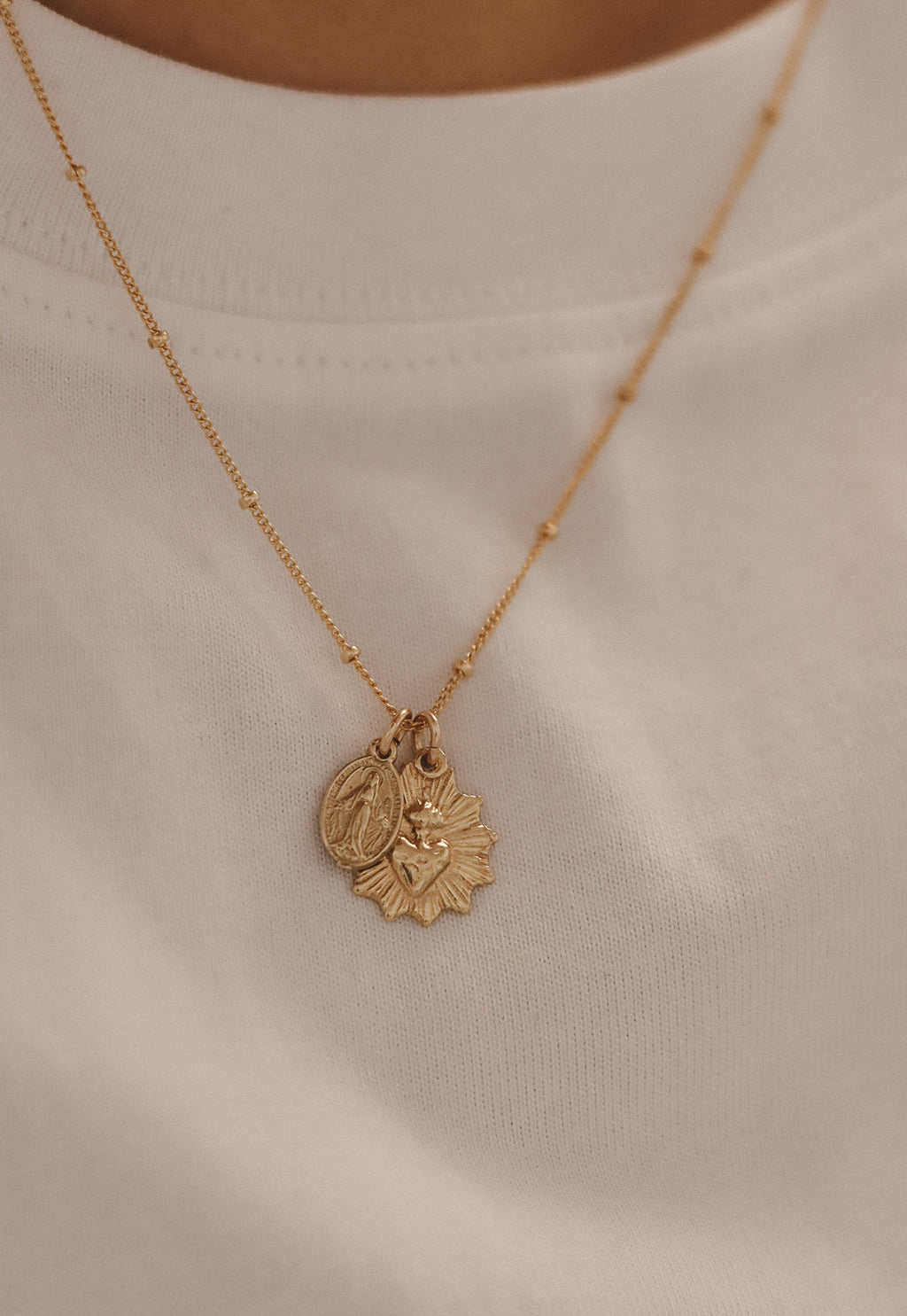 Gold-tone pendant necklace with sacred heart medal charm over white top