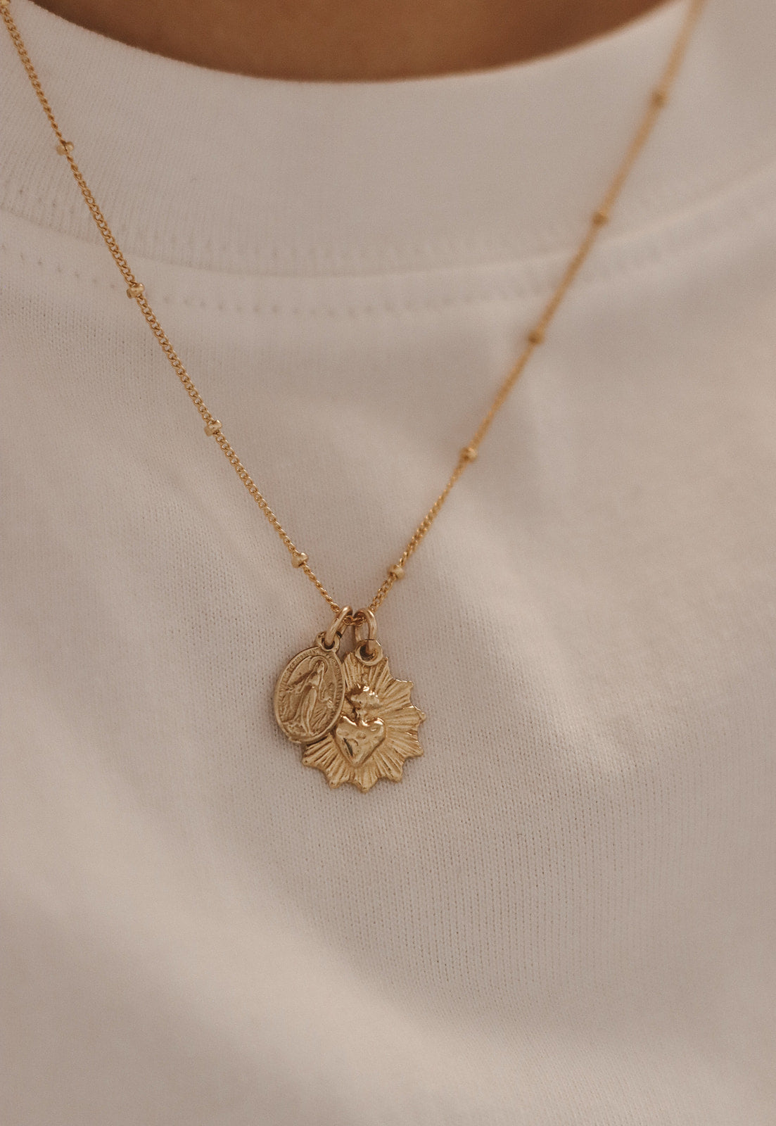 Gold-tone pendant necklace with sacred heart medal charm over white top