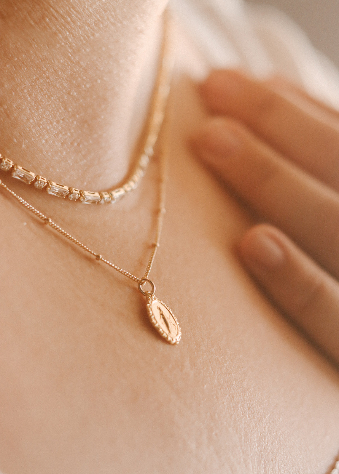 Two delicate gold-tone chains with oval medal charm and clasp detail