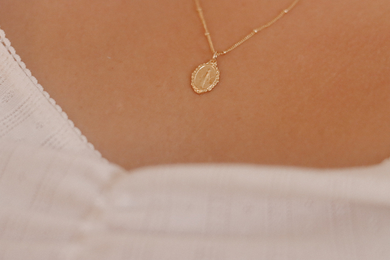 Gold-tone oval medal pendant necklace resting on white fabric neckline