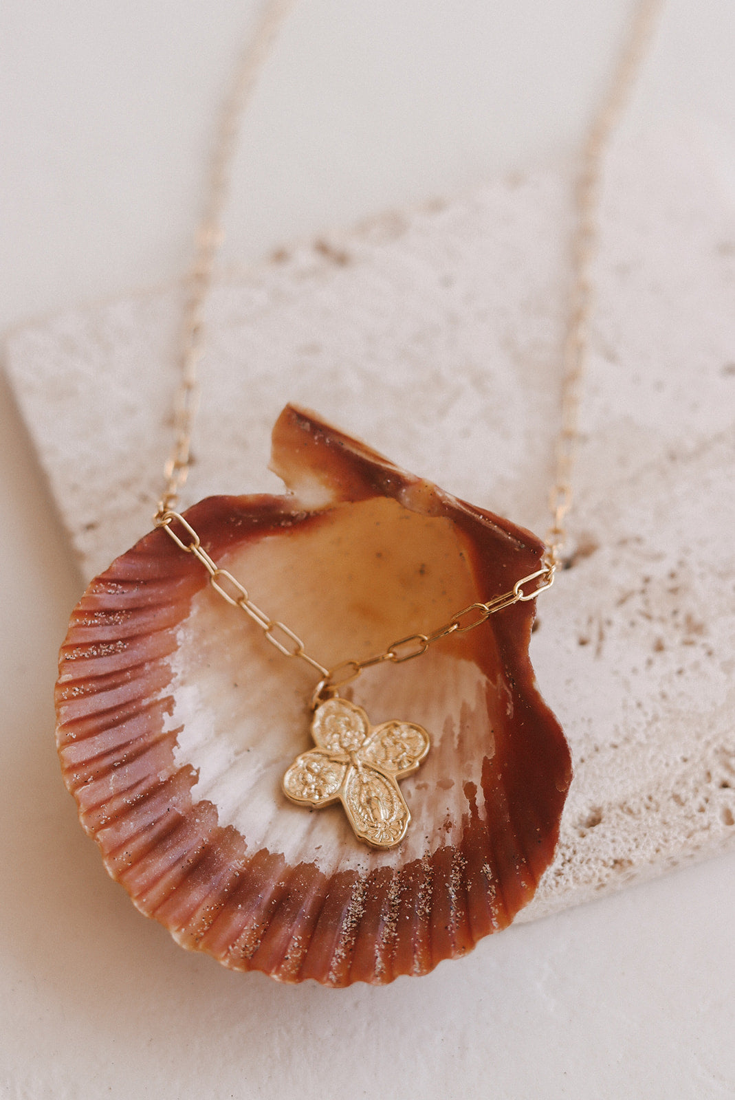 Gold paperclip chain necklace with four-leaf cross charm on seashell