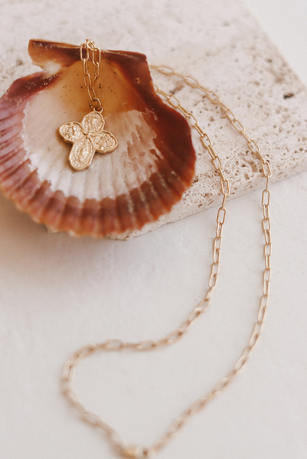 Gold paperclip chain necklace with small cross charm on seashell