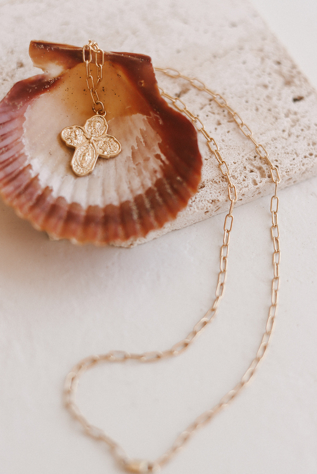 Gold paperclip chain necklace with small cross charm on seashell