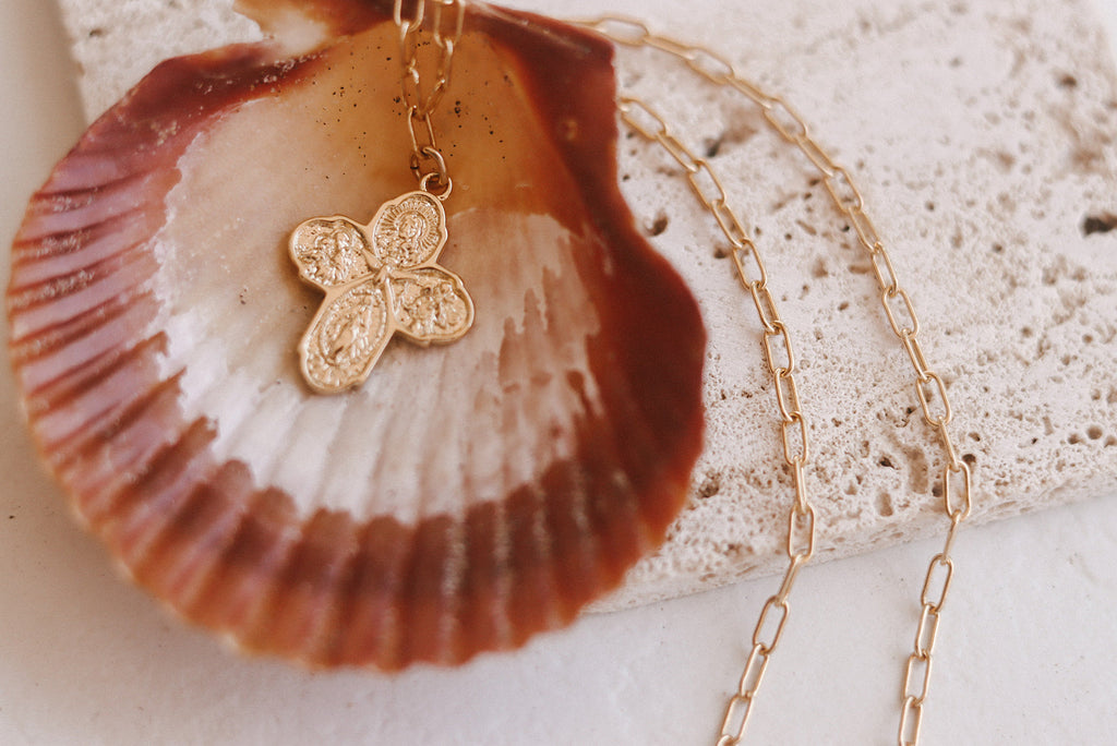 Gold paperclip chain necklace with small four-leaf cross charm on shell