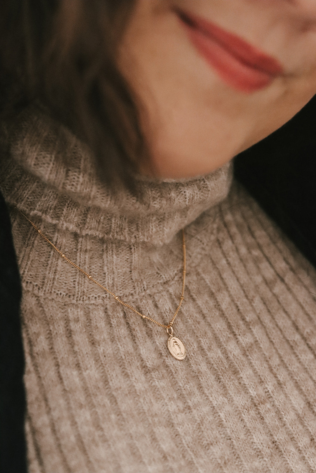 Gold-tone Miraculous Medal necklace with oval pendant on textured knit top