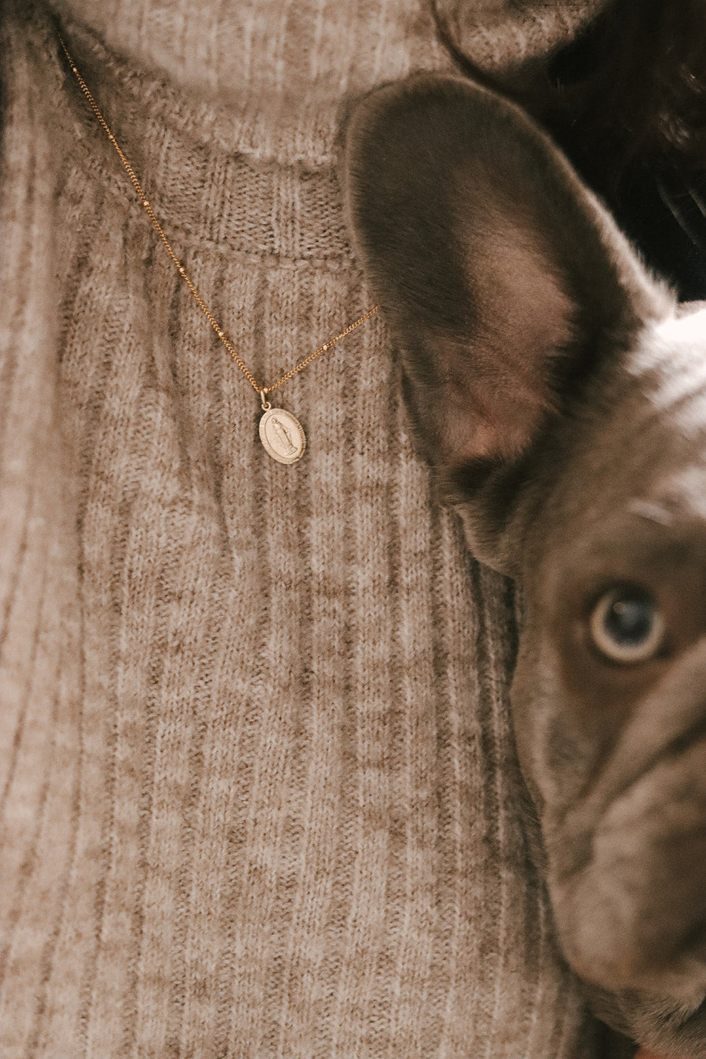 Gold-tone oval Miraculous Medal necklace pendant on knit sweater