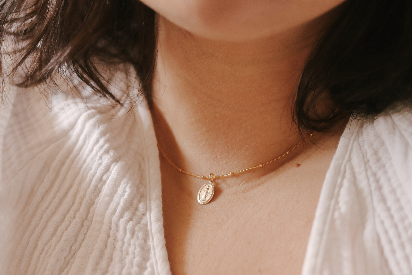 Gold-tone oval Miraculous Medal pendant necklace resting on white knit fabric