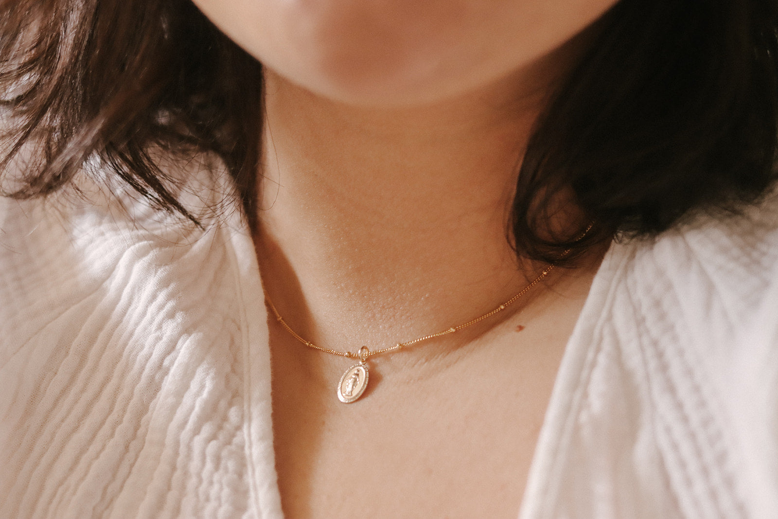 Gold-tone dainty necklace with small oval pendant featuring Mary figure