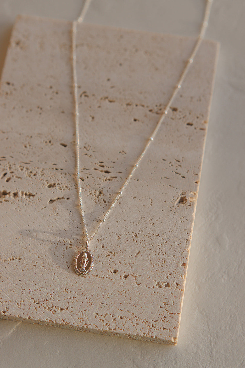 Gold-toned necklace with oval pendant on fine chain, displayed on speckled card