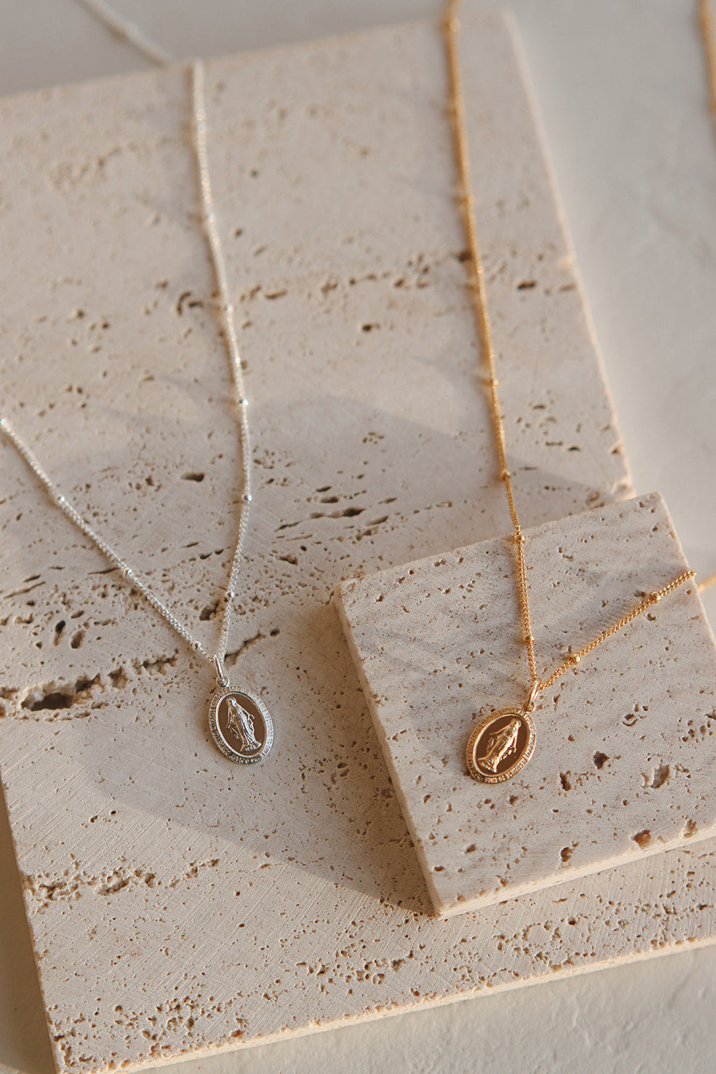 Gold-toned oval medal necklace pendant on thin chain, shown on speckled card