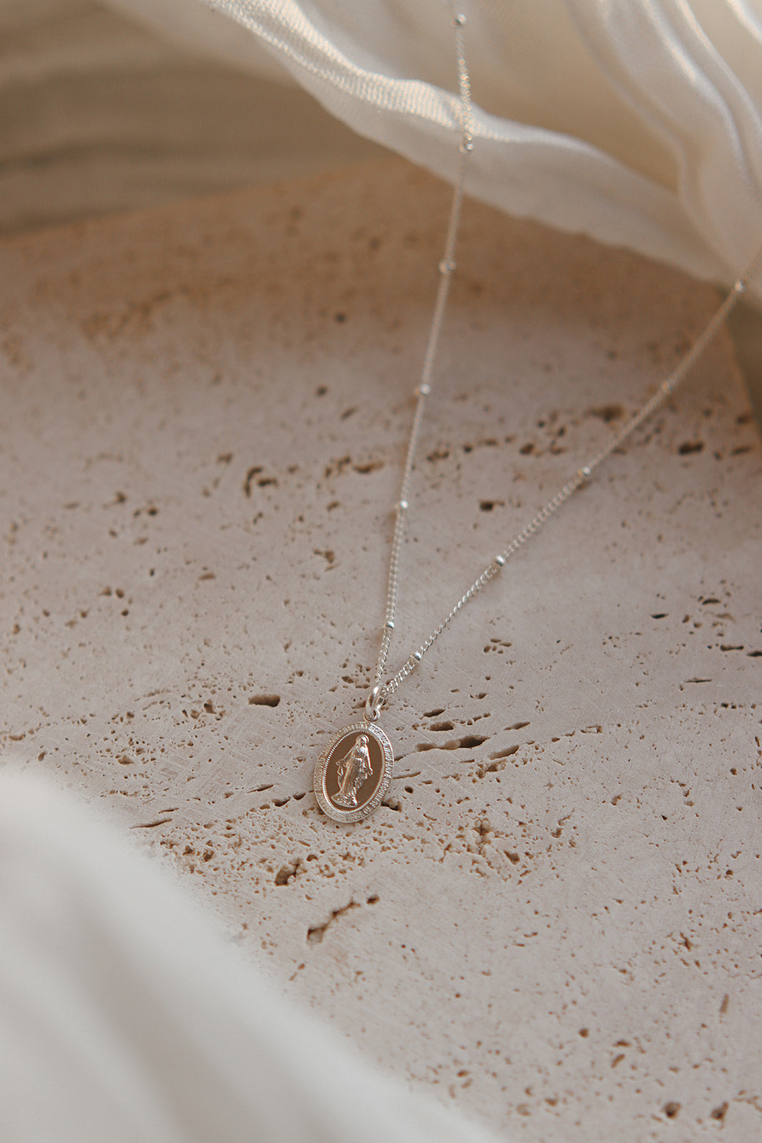 Silver miraculous medal necklace with oval pendant over speckled stone