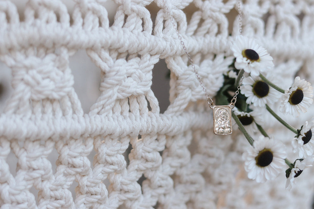 Silver scapular necklace with rectangular saint medal pendant over white crochet