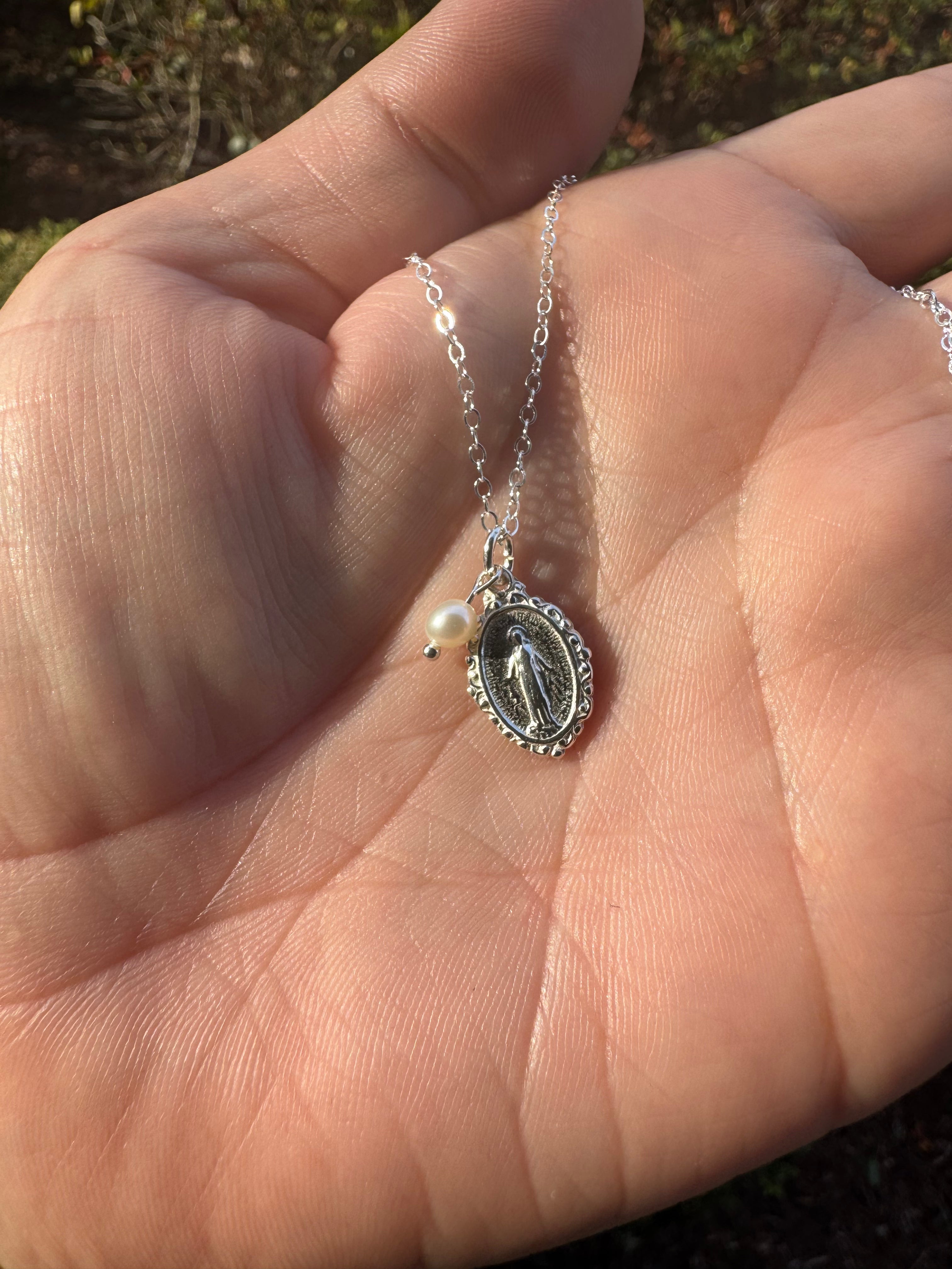 Silver-tone oval miraculous medal pendant necklace held in palm