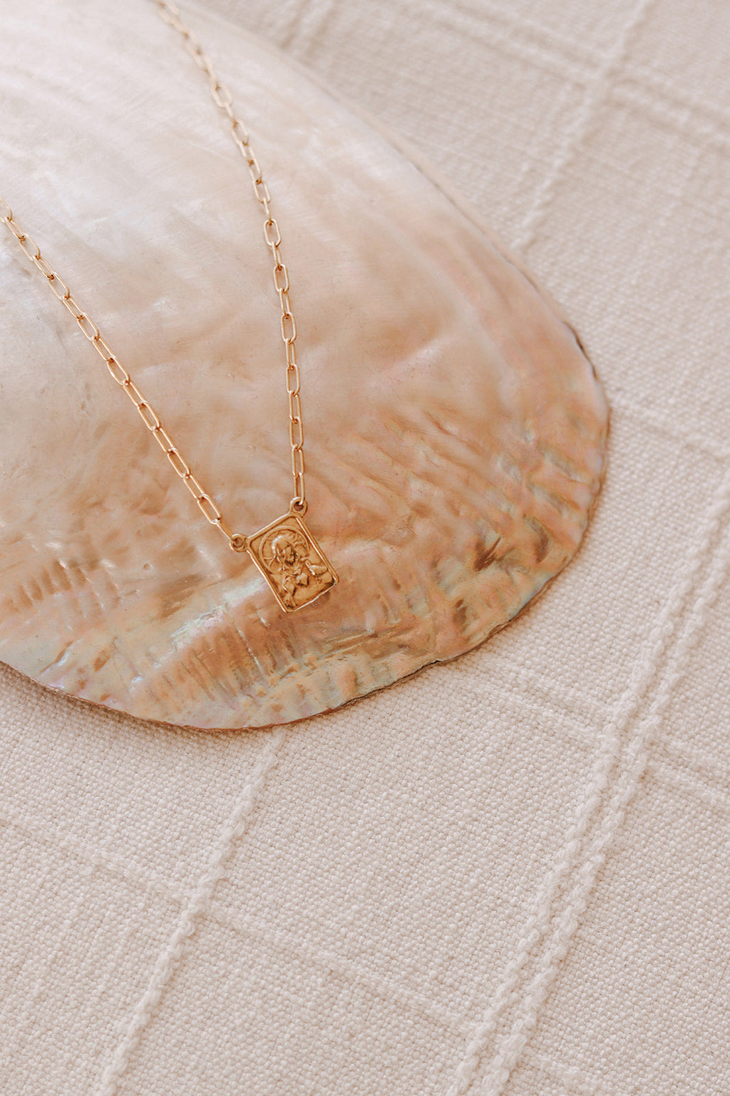 Gold paperclip scapular necklace with square portrait pendant on white fabric