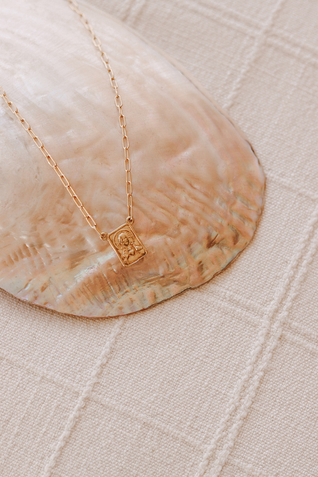 Gold paperclip scapular necklace with square portrait pendant on white fabric