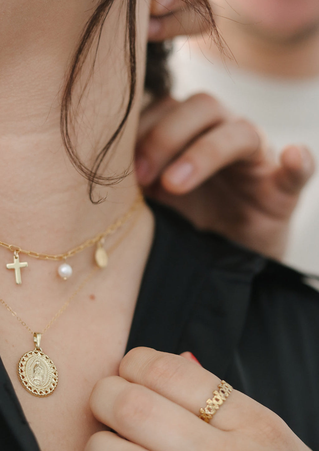 Gold-tone necklace on model’s neck with cross and pearl charms.