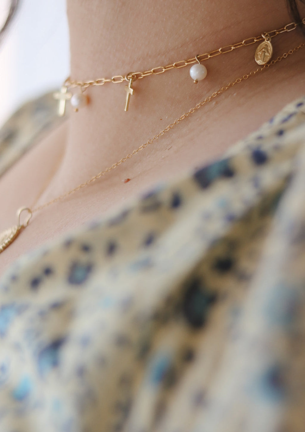 Gold-tone necklace close-up with cross, teardrop pearls, and dangling charms.