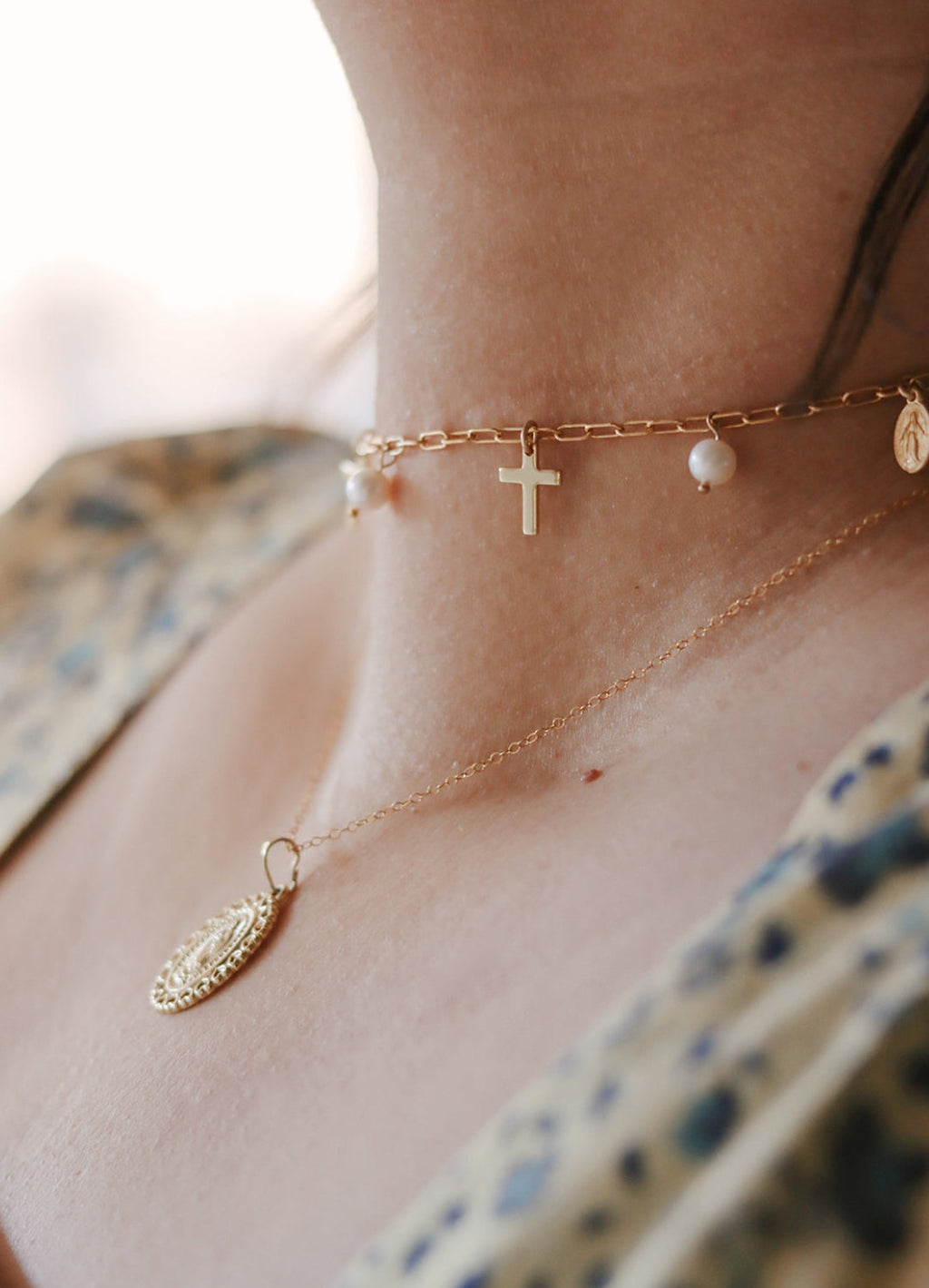 Gold-tone necklace with cross charm and small pearl beads along the chain.