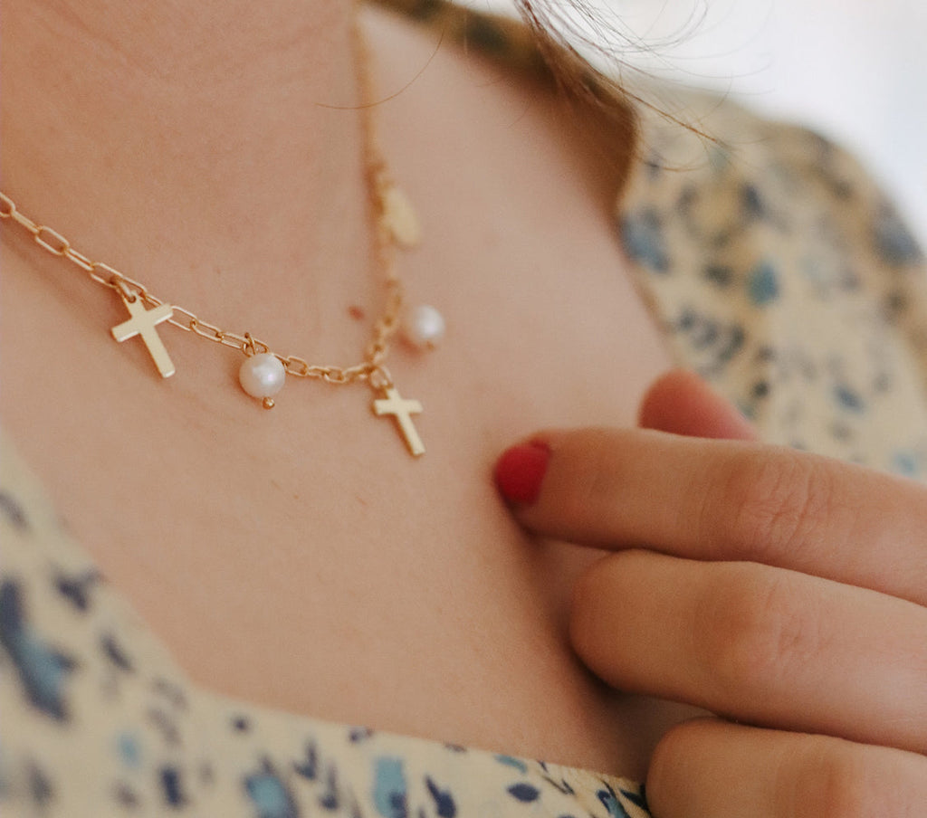 Gold-tone necklace detail with cross charms and pearl dangles.
