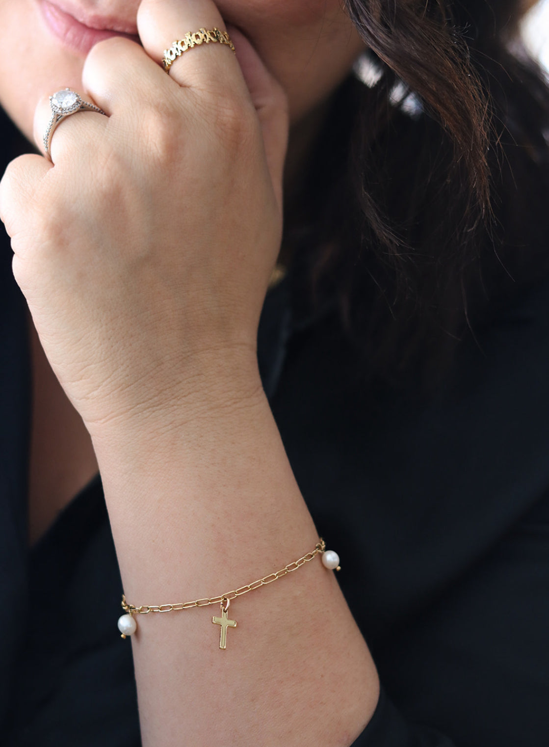 Gold cross charm bracelet with a white pearl bead centerpiece on wrist