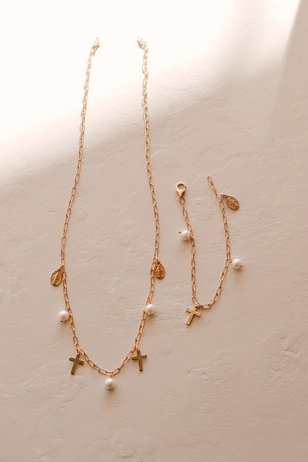 Gold cross charm necklace with pearl beads on layered chain lengths