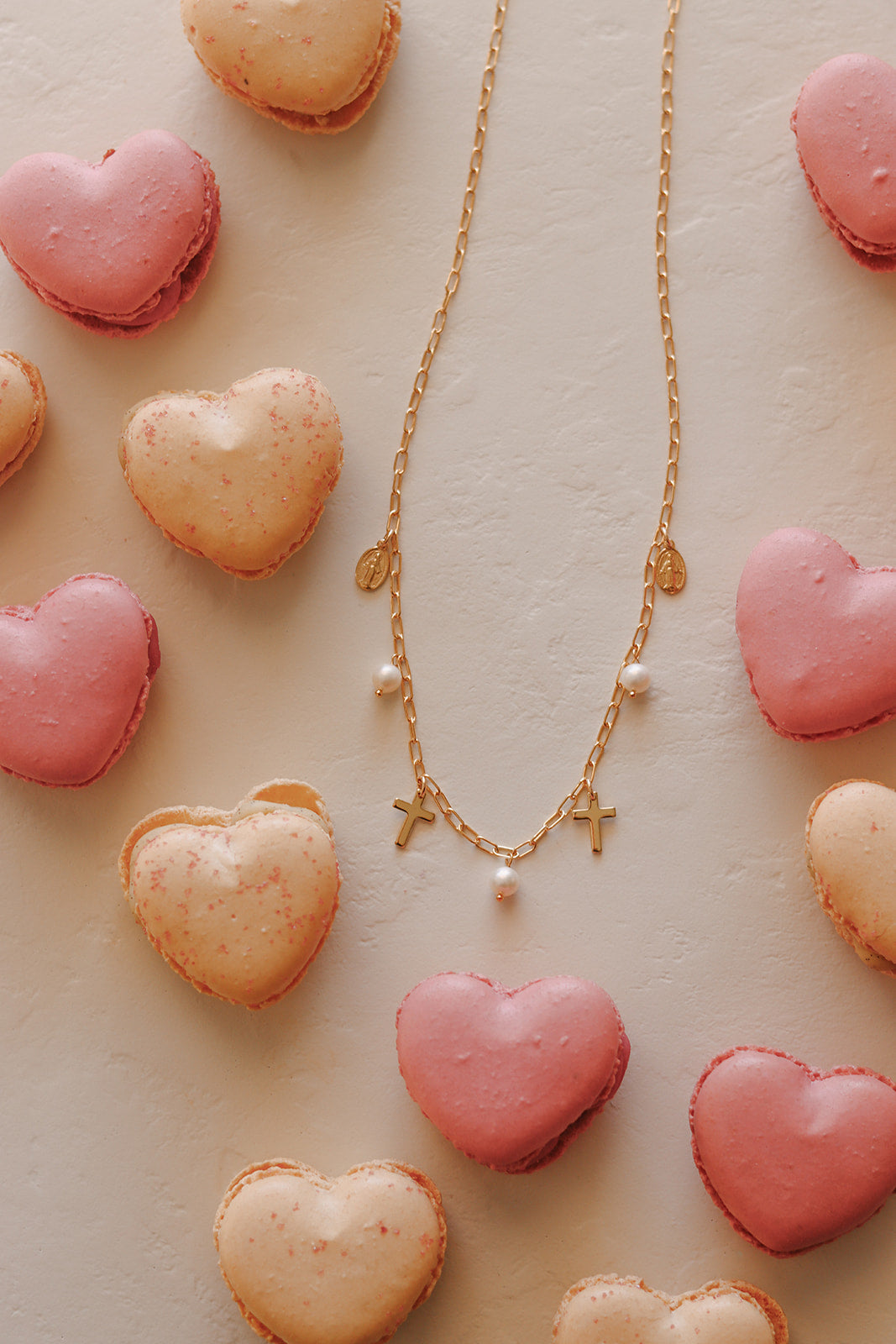 Gold cross charm necklace with pearl beads laid on pink heart shapes