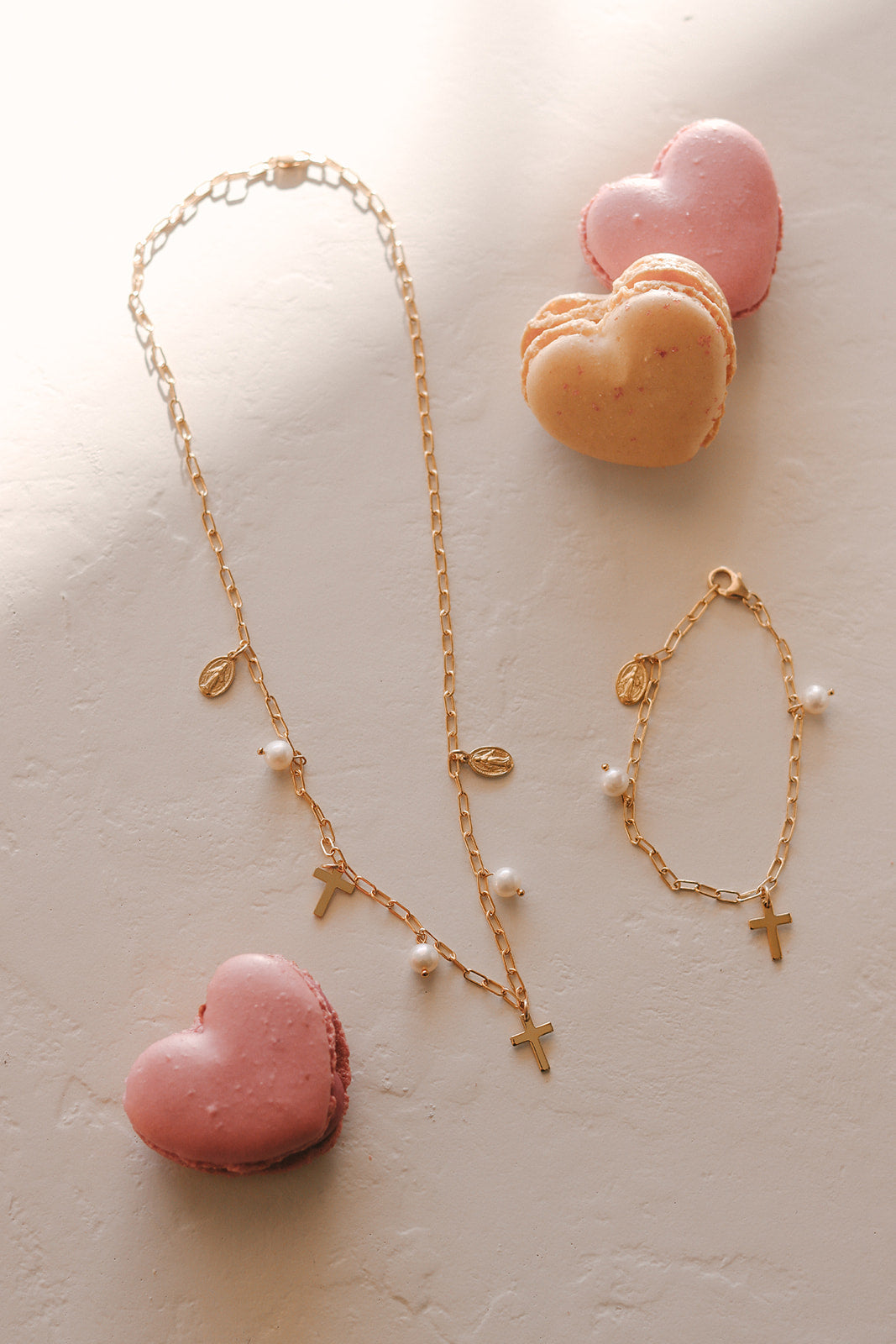 Gold cross charm necklace with pearl beads and multiple heart-themed baubles