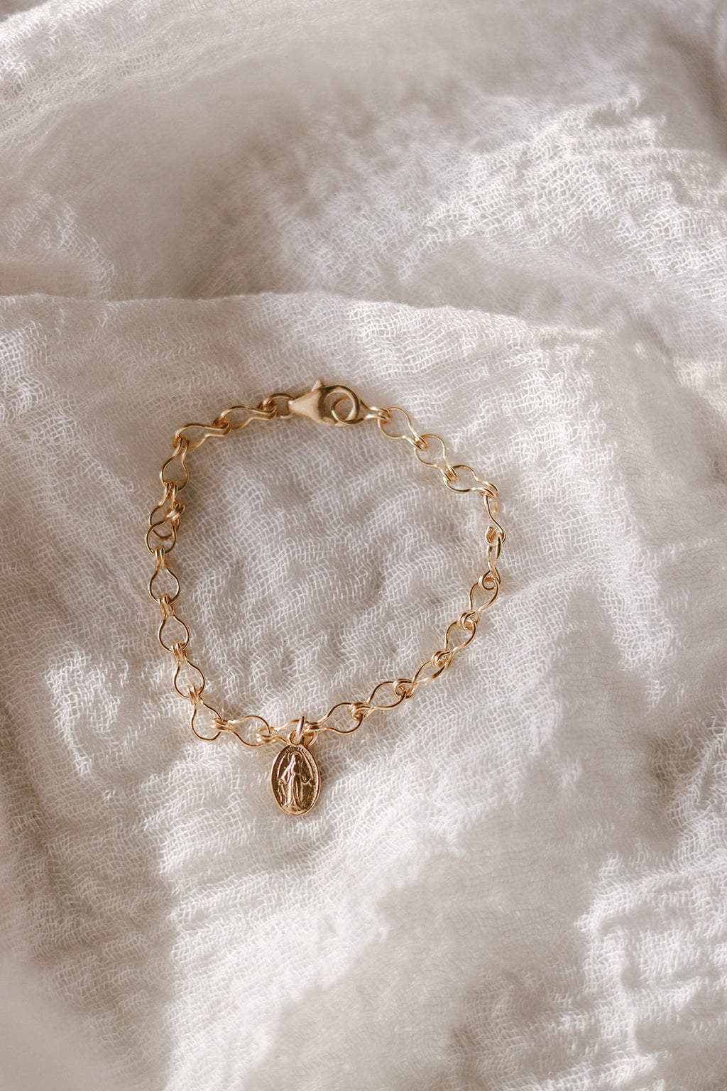Gold-tone bracelet with oval medal charm centered on a delicate chain