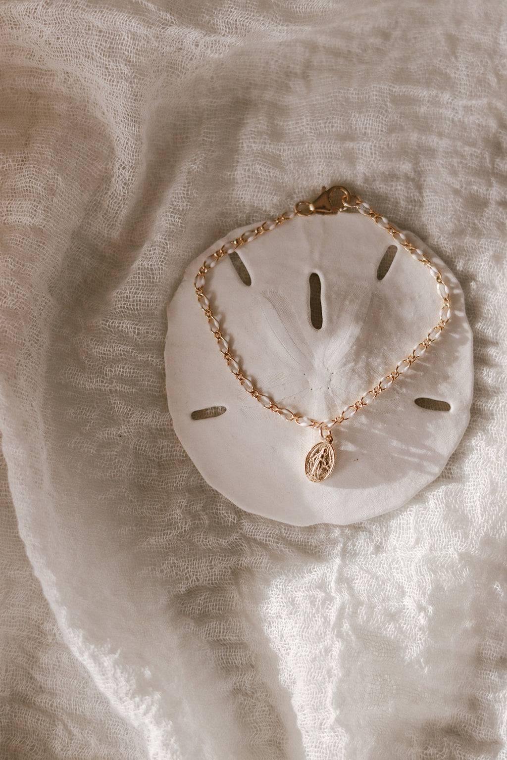 Oval Miraculous Medal bracelet with gold charm on white scalloped backing