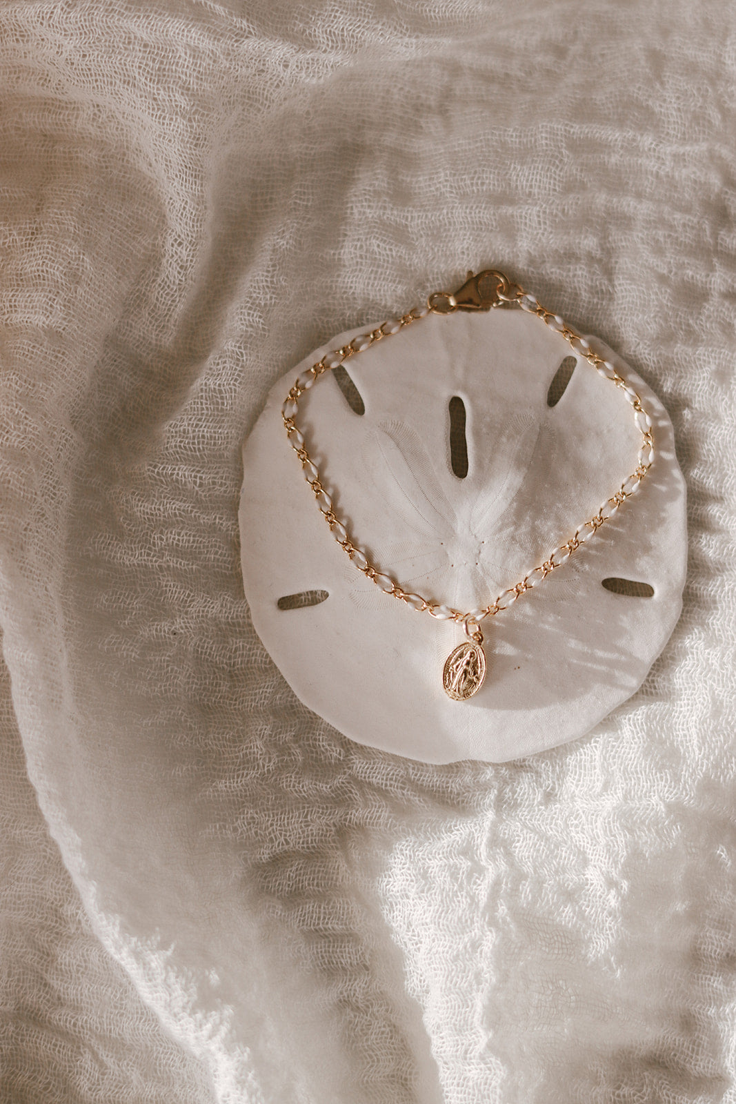 Oval Miraculous Medal bracelet with gold charm on white scalloped backing