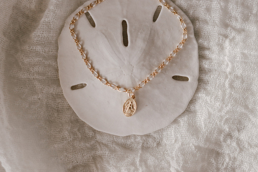 Close view of Miraculous Medal bracelet with gold charm on white backing